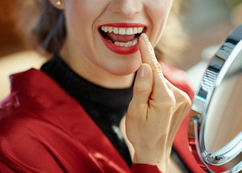 Woman with red lipstick inspecting her teeth in a small mirror