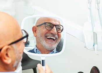 Patient with glasses smiling at reflection in handheld mirror