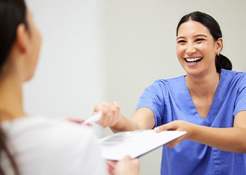 Dental assistant smiling while handing patient form