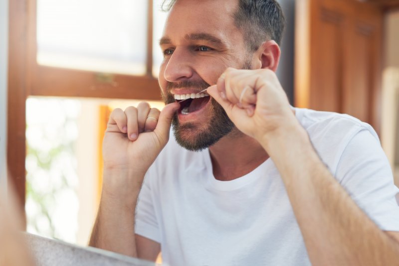 A happy, smiling man flossing between his teeth